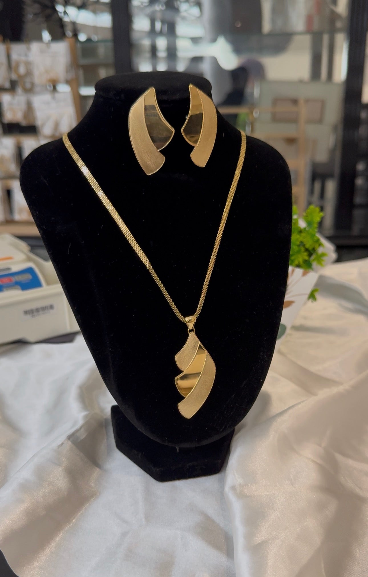 Gold necklace and earrings on a black velvet stand with a blurred background
