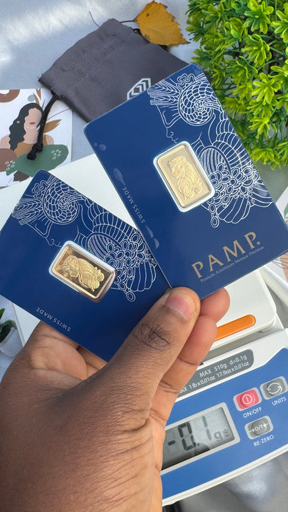 Gold bars in blue PAMP packaging held by a hand with a scale and plant in the background.