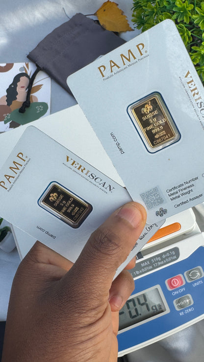 Hand holding a gold bar with 'PAMP' branding against a background of similar bars and a digital scale.