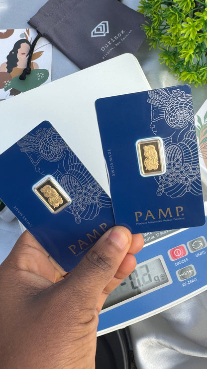 Gold bar on a PAMP card held by a hand with a digital scale in the background.