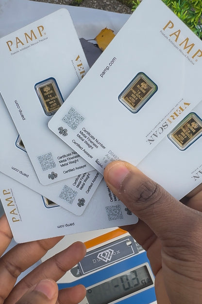 Gold bars in PAMP packaging held by a hand with a digital scale in the background.